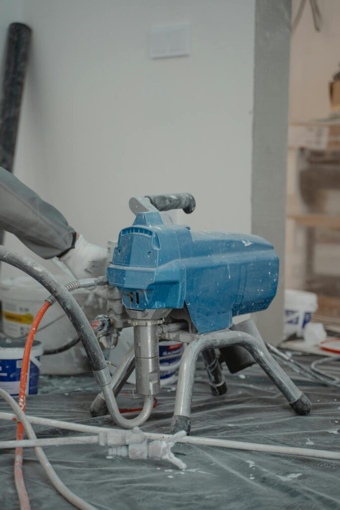 Close-up view of a blue industrial paint sprayer amidst renovation materials in an indoor setting.